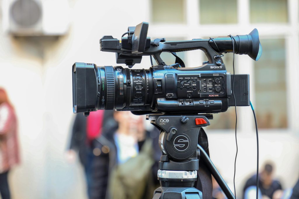Close-up of a Sony video camera mounted on a tripod for outdoor filming.