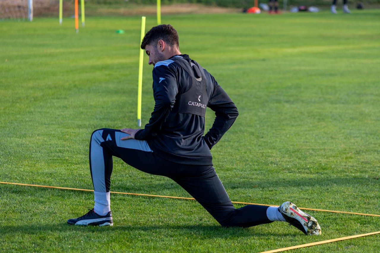 Football player stretching during outdoor training on a sunny day.