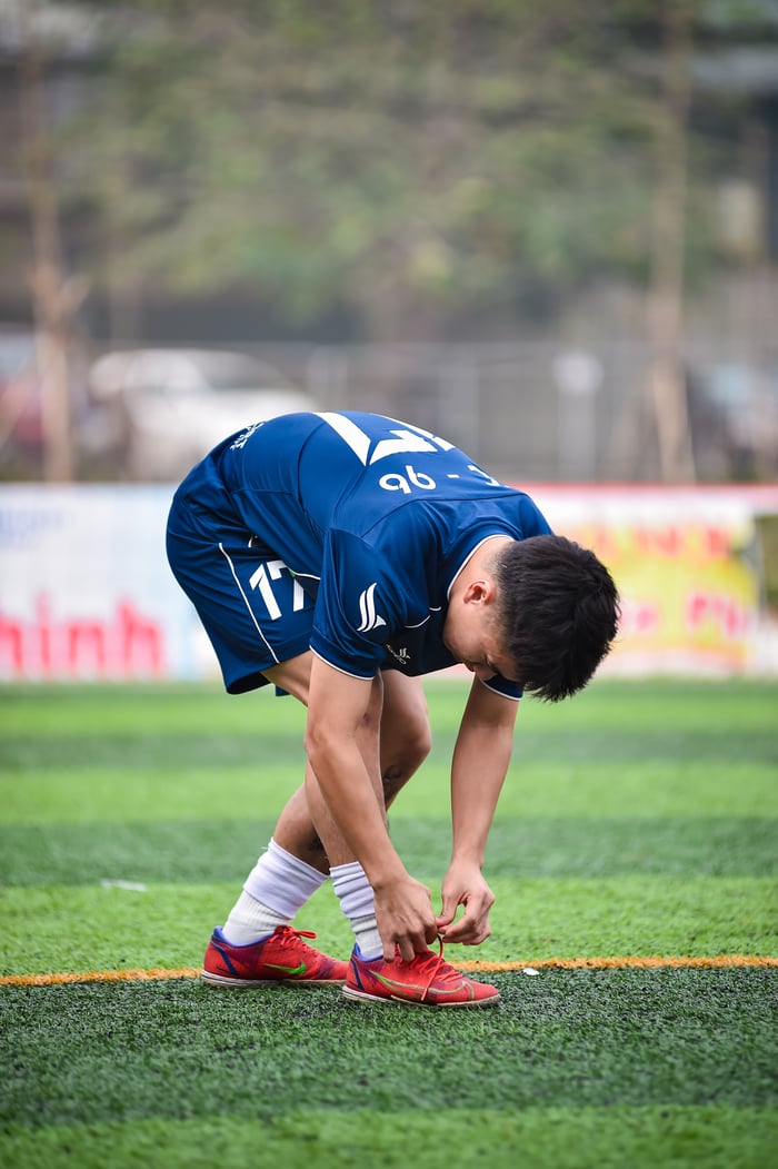 Young male athlete tying shoelaces on a soccer field in Hà Nội, Vietnam.